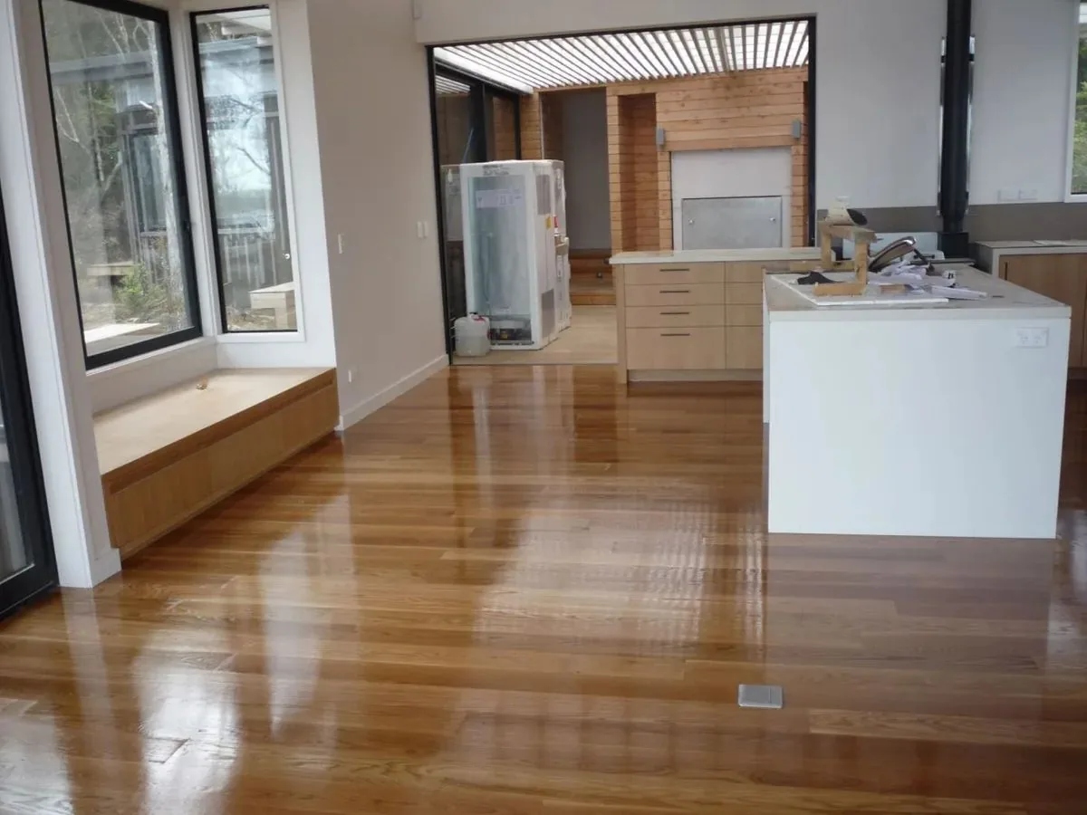 Glossy coated timber floor running past a white kitchen island towards a window seat