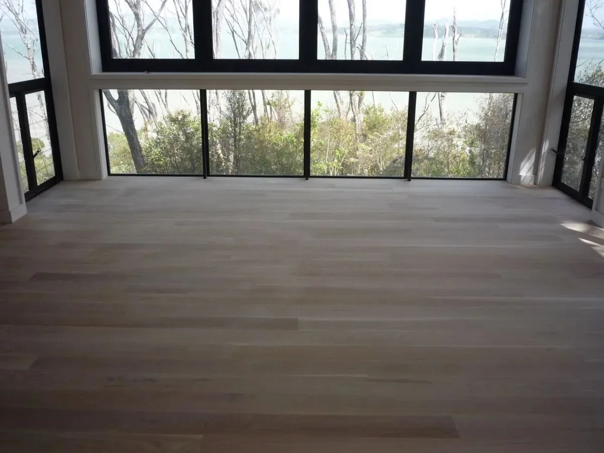 Wide pale timber floor in front of a corner window looking out over trees and water