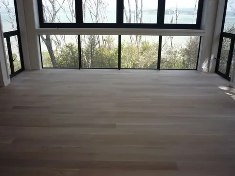 Wide pale timber floor in front of a corner window looking out over trees and water