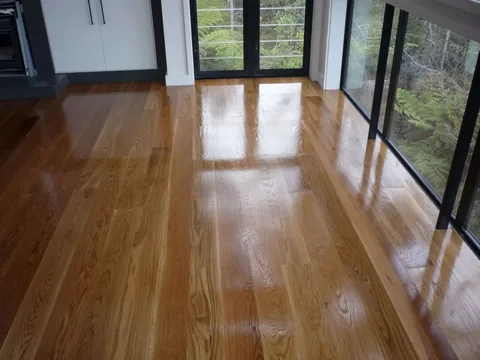 Finished light oak floor reflecting a wall of windows and bush outside