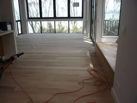 Pale sanded timber floor in a room with a full-height black-framed window wall, a sander and orange extension lead still on the floor