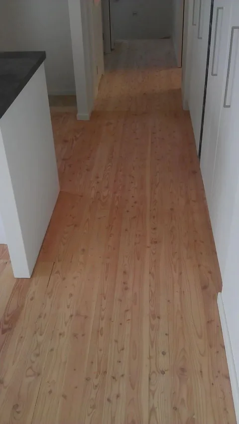 Finished pale timber floor running from a kitchen bench along a hallway past white doors