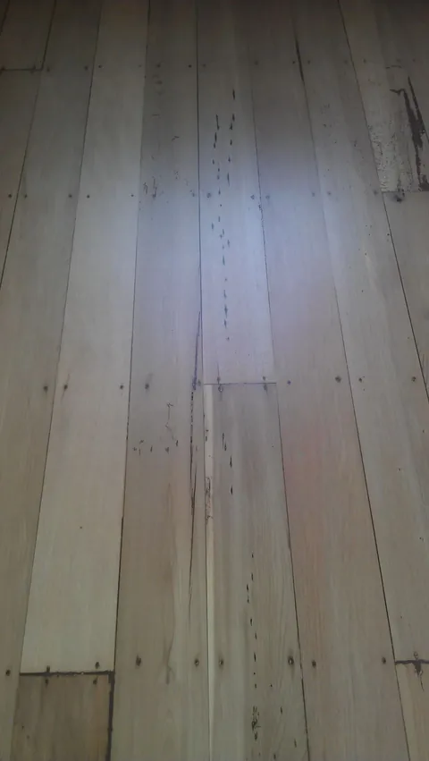 Wide raw sanded floorboards with the nail lines and knots showing clearly