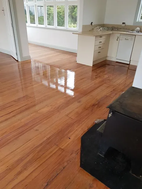 Finished timber floor with a deep gloss coat beside a black fireplace and a white kitchen