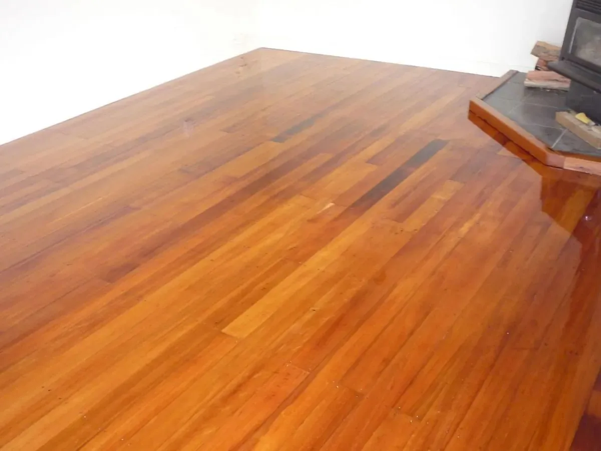 Freshly coated rimu floor running the length of an empty room, the gloss finish catching light from a window off to the right