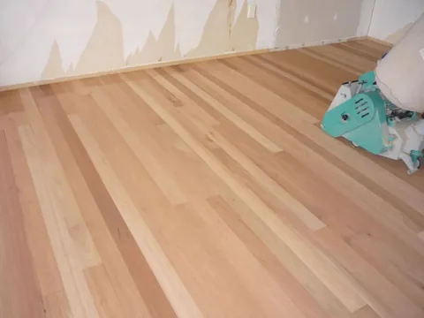 Pale freshly sanded timber boards with a green edging sander parked against the skirting