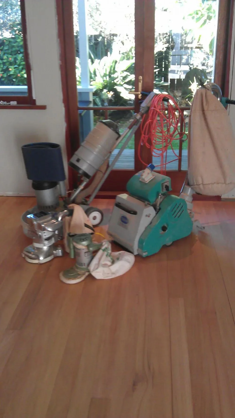 Floor sanding machines, edger and dust bags set out on a finished timber floor in front of open doors